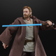 An action figure of Ewan McGregor as Obi-Wan Kenobi, wearing a cloth cloak, raises his blue lightsaber.